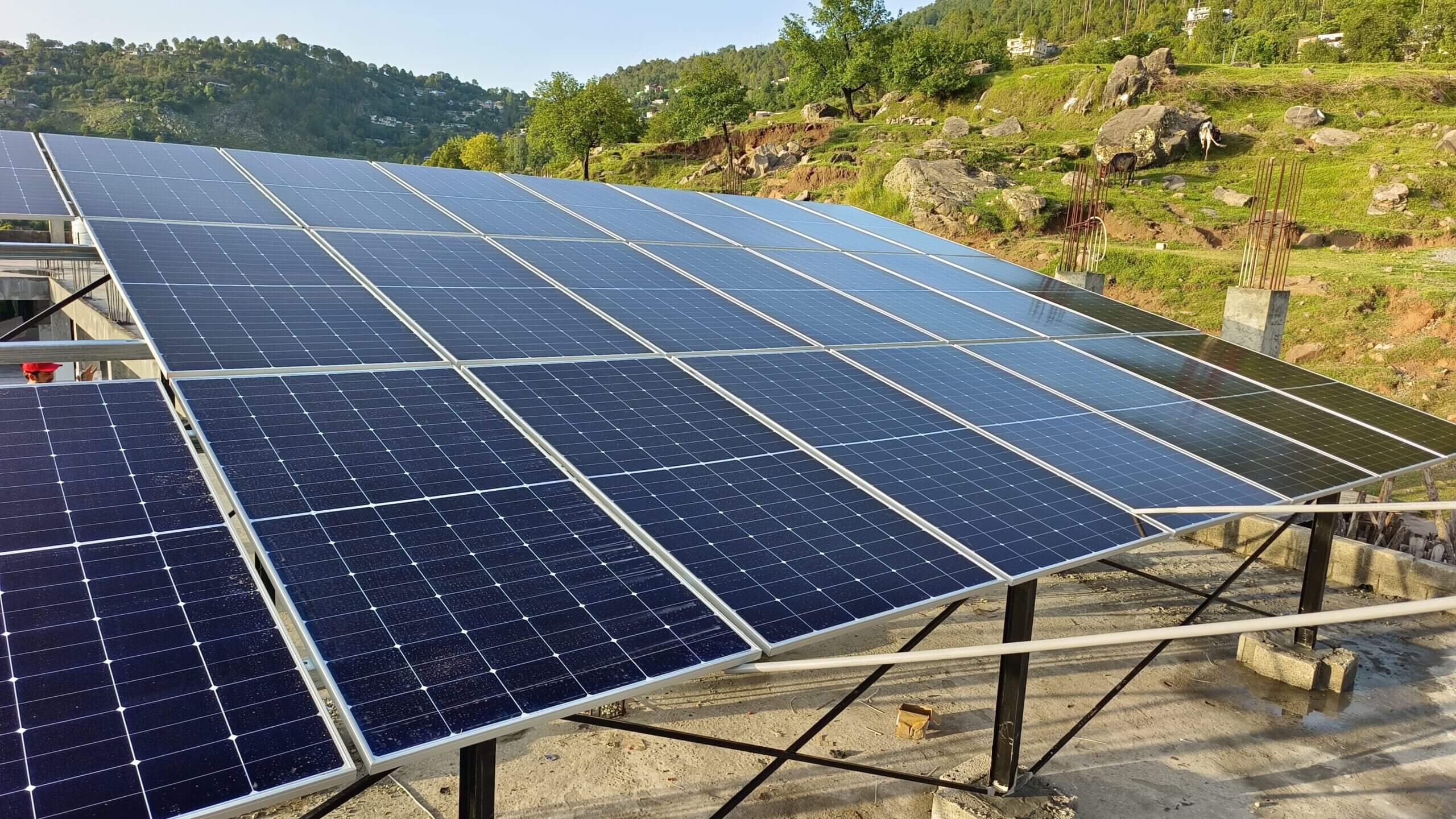 Solar panel array on a rooftop in Murree, Pakistan. Green hills visible in the background.