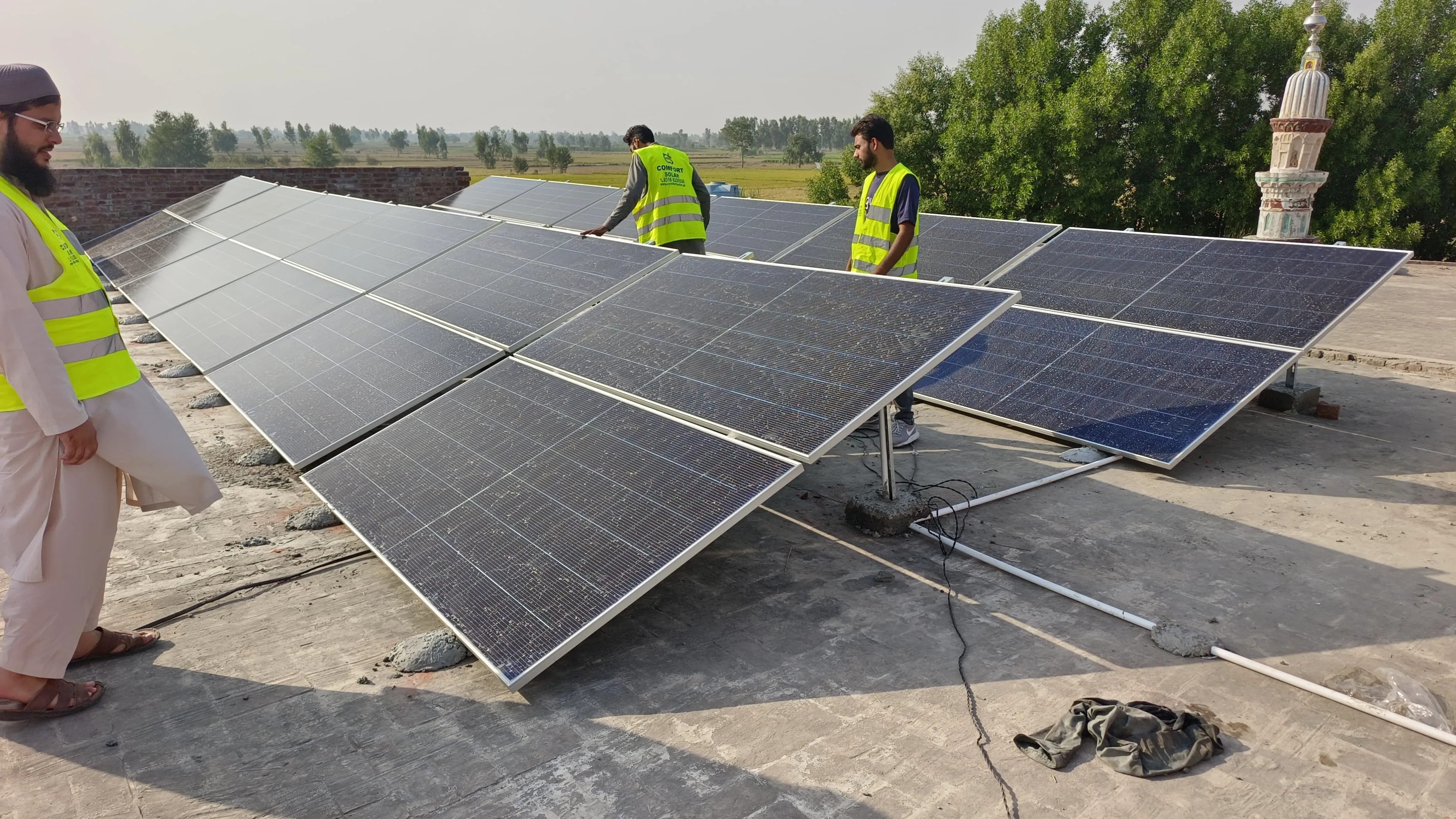 Solar panels being installed on a rooftop by workers wearing safety vests near a mosque.