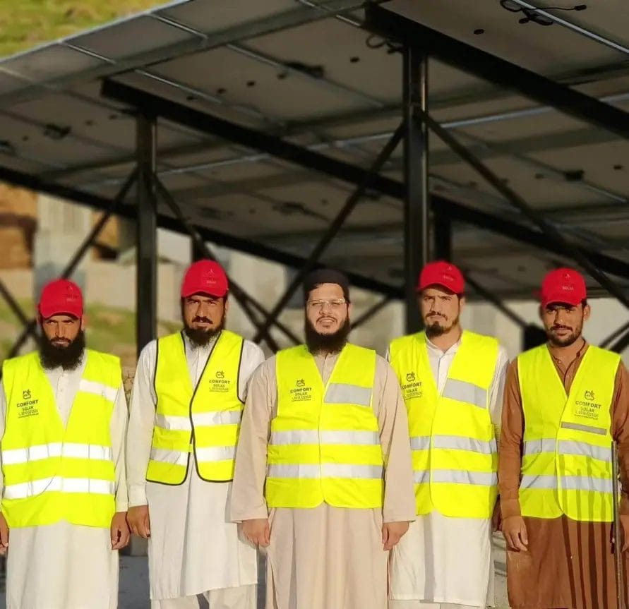 Solar installation team in vests and red caps standing in front of panels.